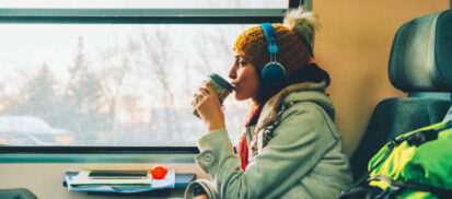 Woman on a train with headphones sipping coffee