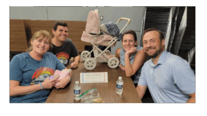 Four adult team members seated around table with baby carriage