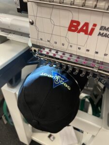Embroidery machine stitching onto a baseball cap.