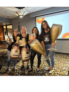 four adults standing with wine and champagne shaped balloons